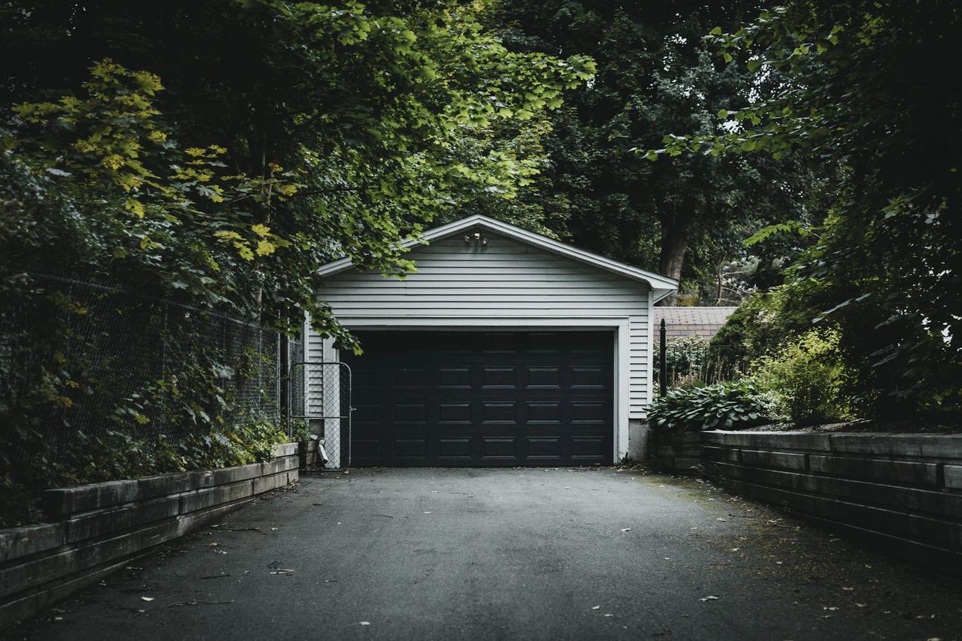 Detached garage with a dark door at the end of a driveway